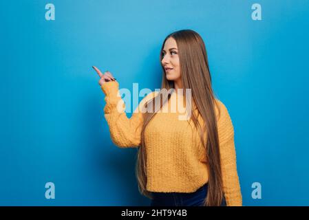 Smiling woman pointing to the side and showing something while standing on an isolated background. Stock Photo