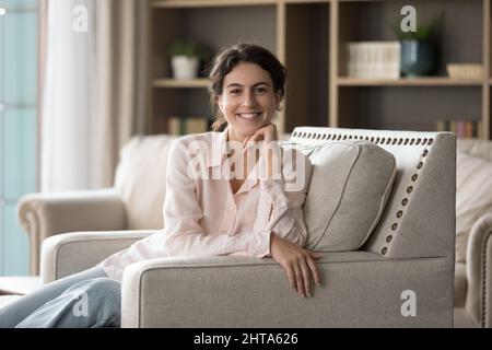 Portrait of smiling young Hispanic woman resting on couch. Stock Photo