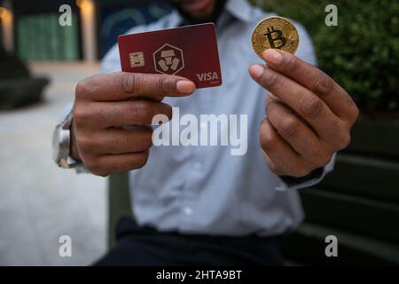 a man holds a Bitcoin coin and the card of Crypto.com, a very popular Cryptocurrency exchange Stock Photo