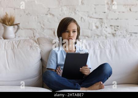 10s boy sitting on couch holding digital tablet looking bored Stock Photo