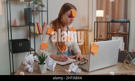 Exhausted woman freelancer with pasted stickers using laptop having concentration problem in office Stock Photo