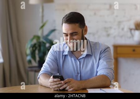 Businessman sits at table hold smart phone enjoy online chat Stock Photo