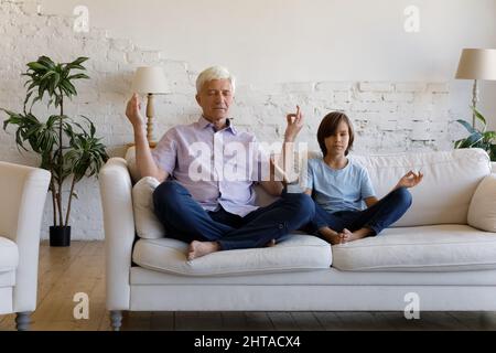 Grandfather and little grandson do meditation practice seated on sofa Stock Photo