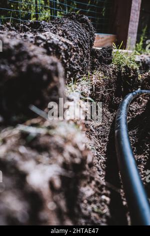 Focus on a black 1 inch sprinkler plastic water line laid in a shallow trench Stock Photo