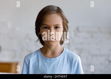Serious sulky 10s boy standing alone indoors looking at camera Stock Photo