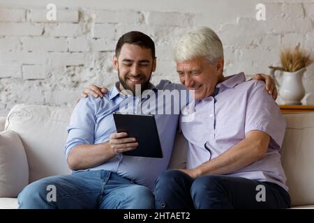 Happy older man his young adult son using digital tablet Stock Photo
