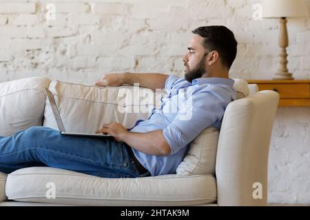 Side view serious man sit on couch with laptop Stock Photo