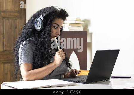 Closeup of a young Hispanic woman wearing headphones and watching something on her laptop Stock Photo