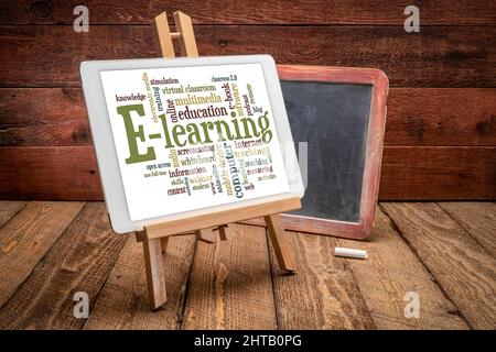 online education concept - e-learning word cloud on a digital tablet replacing a slate blackboard in a rustic retro classroom Stock Photo