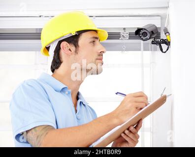 Contracted to secure your home. Shot of a handsome young man installing a security camera. Stock Photo