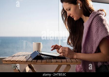 Young woman in headphones is checking email on tablet on balcony on vacation Stock Photo
