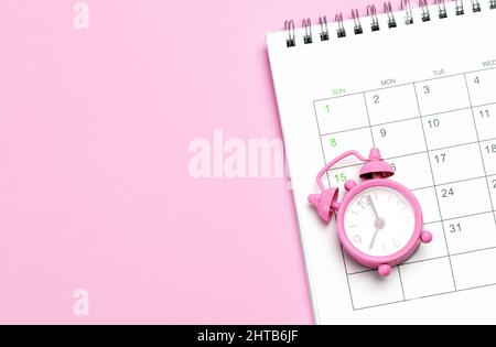 Pink alarm clock and calendar on a pink background. Concept days of menstruation or menopause. Template Copy space for text. mock-up. Stock Photo