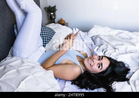 Young latin woman reading book and studying on bed at home in Mexico Latin America Stock Photo
