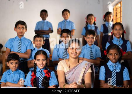 Happy smiling Kid with teacher prepared for class group photo or picture at classroom by looking at camera - concept of last day of school, childhood Stock Photo