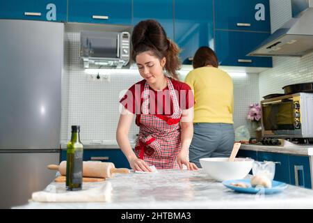 Housekeeping and cleaning. Two young women prepare food together in the kitchen. Woman in the foreground wipes the table. Stock Photo