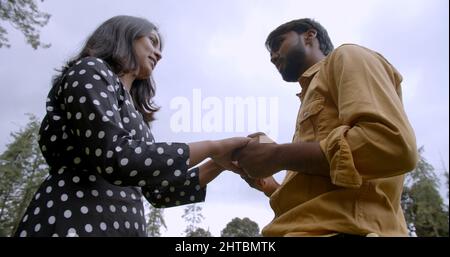 Shallow focus of a lovely South Asian young adult couple holding hands and dancing in a park Stock Photo