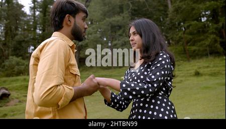 Shallow focus of a lovely South Asian young adult couple holding hands and dancing in a park Stock Photo