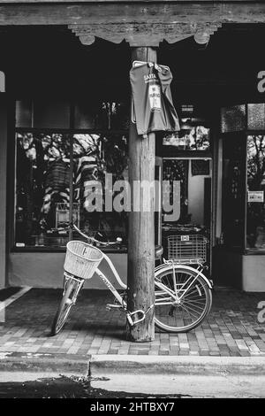 Vertical grayscale shot of a bike chained up to a wooden pillar with a no parking sign on it Stock Photo