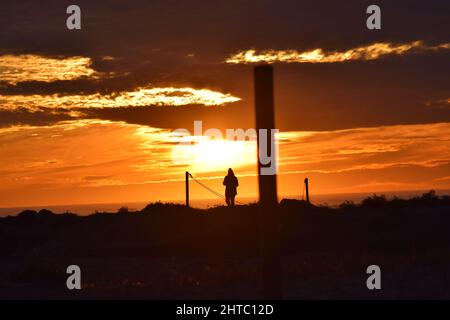 An alone man standing on a hill looks at the yellow sunset with cloudy sky on the background Stock Photo