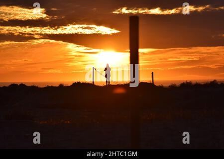 Man standing on a hill looks at the yellow sunset with cloudy sky on the background Stock Photo