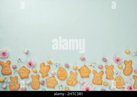 Bunny shaped sugar cookies with Easter chocolate eggs and flower background. Happy Easter Stock Photo