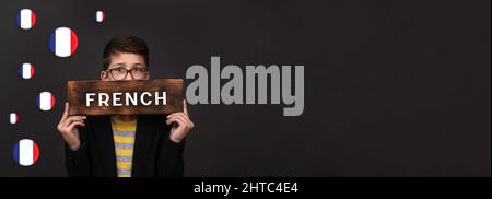 learning French. banner on a black background. a teenager holds an advertising sign for language courses. copy space Stock Photo