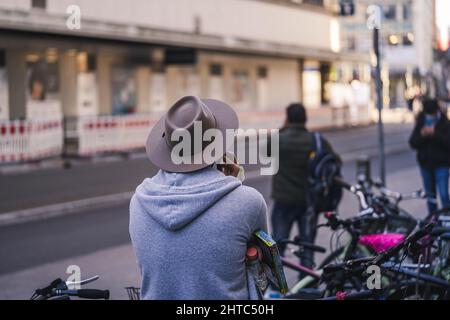 Back shot of a Man with hat and hoodie making a phone call in the street of Munich, Germany Stock Photo