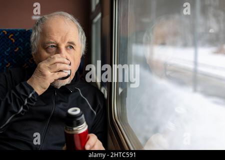 Senior man enjoying fresh tea during travel by train during winter time, traveling concept Stock Photo