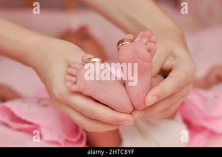 the baby's legs are in the mother's hands. gold wedding rings on baby's toes. family or wedding concept Stock Photo