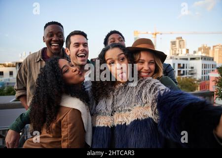 Cheerful multi-cultural group of friends taking a selfie on a rooftop terrace, posing with friends at rooftop party Stock Photo