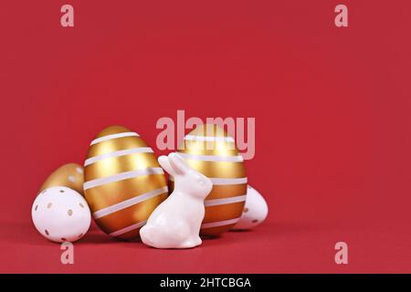 Easter bunny figure and golden and white easter eggs with stripes and dots on dark red background with copy space Stock Photo