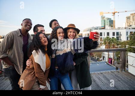 Multi-cultural group of friends taking a selfie at a rooftop party. Posing with young adult friends. Stock Photo