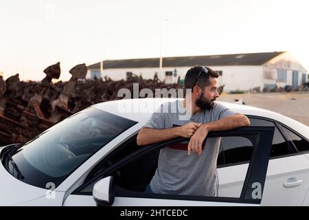 attractive bearded young man resting leaning against the door of his car, road trip and driving concept, copy space for text Stock Photo