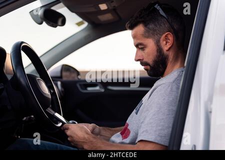 attractive bearded young man using his mobile phone sitting resting inside his car, leisure and technology of communication concept Stock Photo