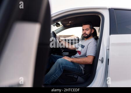 handsome bearded young man looking serious at camera sitting behind the wheel of his car, leisure and driving concept Stock Photo