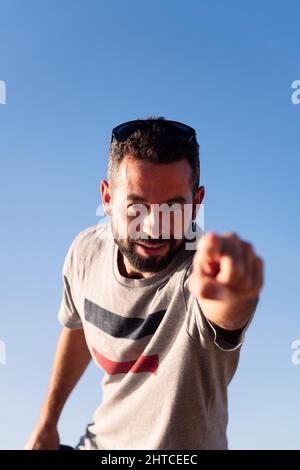 vertical photo of a bearded man pointing finger at camera with blue sky in background, copy space for text Stock Photo