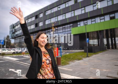 Young cheerful Caucasian lady greeting someone wearing a suit in front of a building Stock Photo