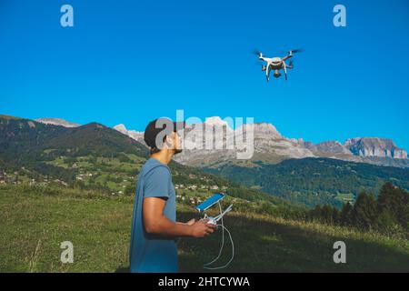 Young man flying drone on amazing mountain landscape. Man operating a drone with remote control taking aerial photos and videos. Stock Photo