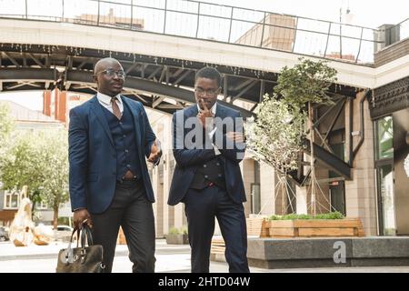 Two dark-skinned african american businessmen in suits with briefcases walk along the city street Stock Photo