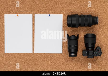 Cork board with photo camera, two lenses and white paper hanging on a thumbtack Stock Photo