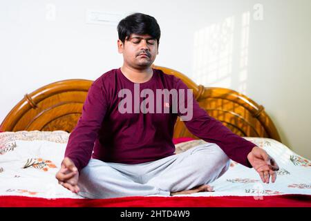 Young indian man doing meditation with eyes closed on bed- concept of healthy lifestyles, mindfulness and strees relief Stock Photo