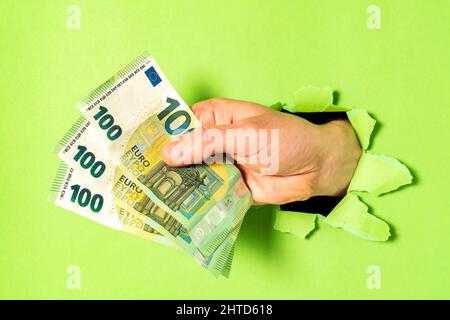 Businessman breaking through green paper with bunch of Euro bills in hand, closeup Stock Photo
