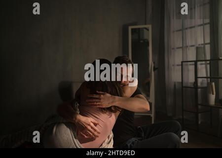 Mid-adult couple sitting on bed at night and hugging. Stock Photo