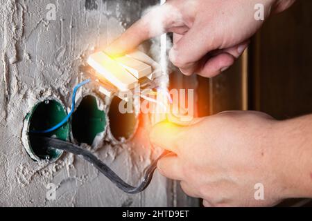 A man holds on to electrical wires and an electrical switch. Electric shock, flash of fire and smoke. Safety Stock Photo