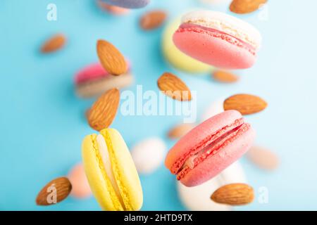 Multicolored flying macaroons and almonds eggs frozen in the air on blurred blue background. top view, flat lay, close up. Breakfast, morning, concept Stock Photo
