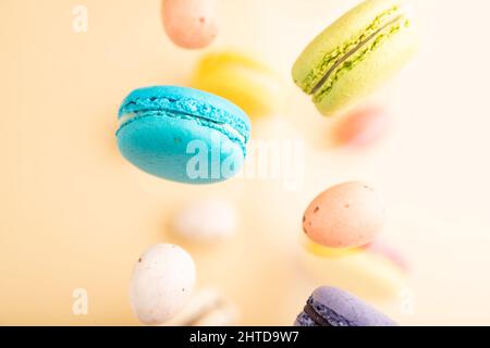 Multicolored flying macaroons and chocolate eggs frozen in the air on blurred beige background. top view, flat lay, close up. Breakfast, morning, conc Stock Photo