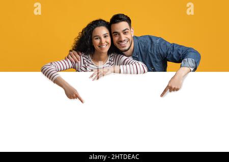 Happy Young Arab Couple Pointing Down At Big White Advertisement Board Stock Photo