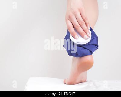 The girl applies a medical ice bag to the ankle joint to eliminate pain and relieve swelling. Treatment of joints with cold for sprains and bruises. C Stock Photo