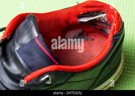 A ripped backdrop in sporty multicolored sneakers. Poor quality shoes, close-up, damaged Stock Photo