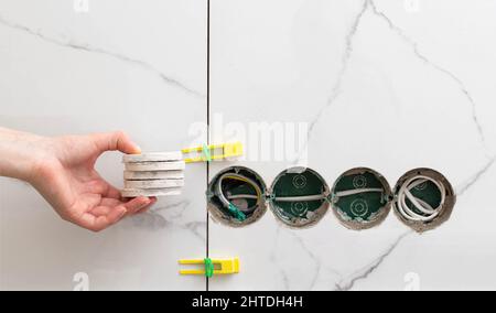 Drilled holes for sockets in the master's hand against the background of porcelain tiles. Repair in the apartment. Copy space for text Stock Photo